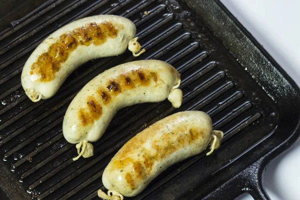 Fried sausages in a black frying pan with grill. Close-up. — Stock Photo, Image
