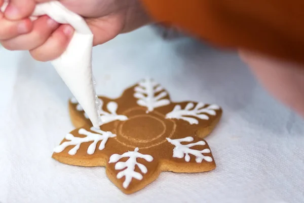 Детские руки украшают пряники в виде снежинки с сахарной глазурью с помощью пакетика. Рождество и Новый год. Выпечка праздничных печенек . — стоковое фото