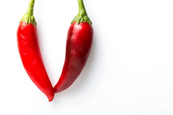 Dos chiles rojos que se tocan forman un símbolo V sobre un fondo blanco . — Foto de Stock