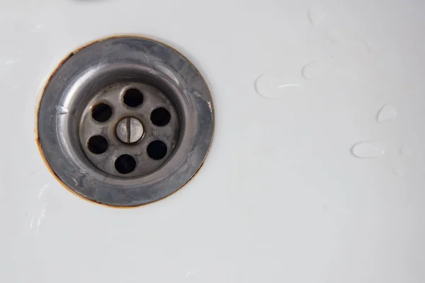 Drain hole with rust around the edges in a white sink or bathtub with drops of water. — Stock Photo, Image