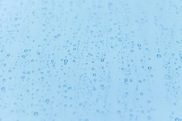 Blauwe achtergrond met regen druppels op het glas. Ondiepe scherptediepte. — Stockfoto