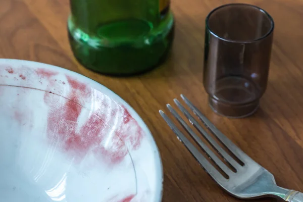 Fingerprints on the edge of the dish are covered with a special powder. A close-up of a plate, a glass, a bottle and a fork with leftovers on the table at the crime scene. — Stock Photo, Image