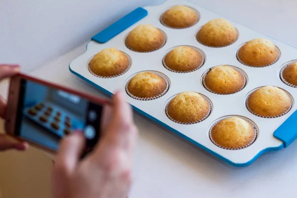 Women's hands take pictures of cooked cupcakes on a mobile phone. Bakery products. — Stock Photo, Image