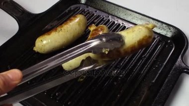 Üç sosis tava içinde yanmış. Forseps ile aşçı el onları ızgara döner. Ağır çekim