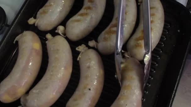 Les demi-saucisses crues sont frites dans une poêle à griller et retournées à l'aide de pinces. SlowMo . — Video