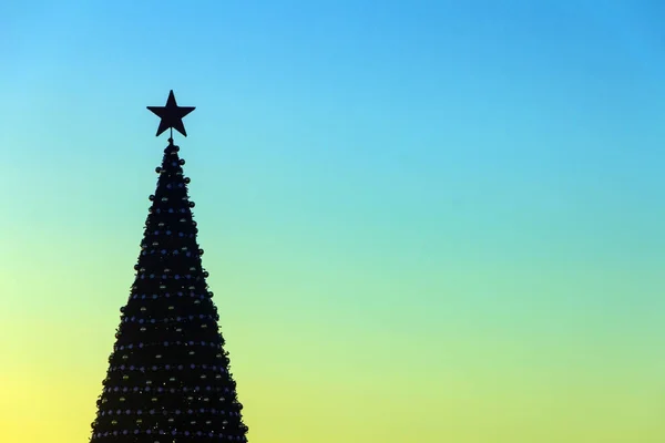 Silueta de un árbol de Navidad decorado con una estrella de cinco puntas en el vértice sobre el fondo del cielo soleado de la mañana. Fondo de celebración . —  Fotos de Stock