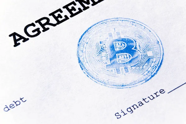 Macro. Blue stamp of virtual currency bitcoin on a loan agreement. The loan agreement, the signature is printed on a white sheet of paper.