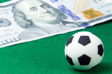 Küçük Top 100 dolar yanında yeşil bir arka plan üzerinde. Kavram para ve spor, Futbol bahisleri. Makro. Süper yakın çekim.