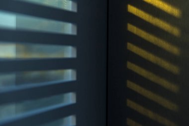 Arka plan. Duvardaki çizgili sabah veya akşam ışık perdeleri üzerinden parlar. Mavi ve sarı sesi.