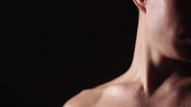 Drops of water or sweat on the body of an athlete. Turning his head. The lower part of the face of an Asian man on a dark background. Close-up. — Stock Video