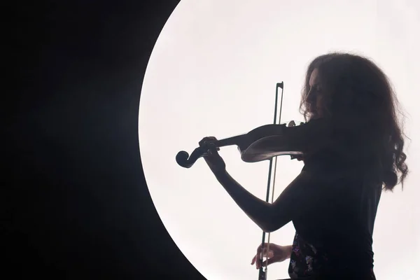 Silhueta de uma mulher violinista em um semicírculo branco com fumaça em um fundo preto. Um conceito para a música durante a lua cheia. Fundo noturno. Espaço de cópia . — Fotografia de Stock