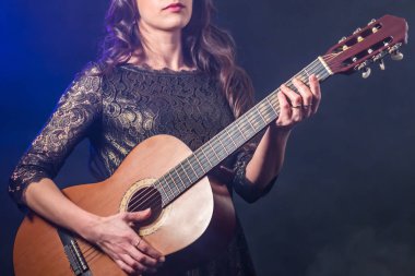Akustik gitar uzun siyah saçlı bir kızla elinde. Dumanlı mavi arka plan.
