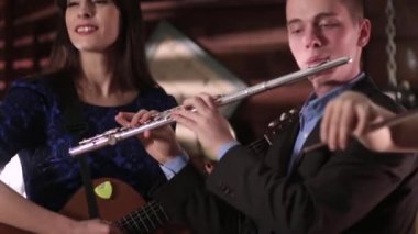 Bir adam bir ceket ve gömlek flüt ve güzel bir esmer mavi bir elbise bir gitar çalmaya çalış. İki kişi müzisyen müzik yeniden.