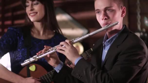 El tipo del traje toca la flauta y la chica del vestido azul toca la guitarra. Concepto musical . — Vídeo de stock