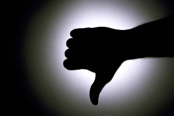 Thumbs down. Silhouette of a mans hand against a background of a bright light circle. Black and white picture. — Stock Photo, Image