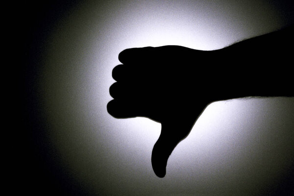 Thumbs down. Silhouette of a mans hand against a background of a bright light circle. Black and white picture.