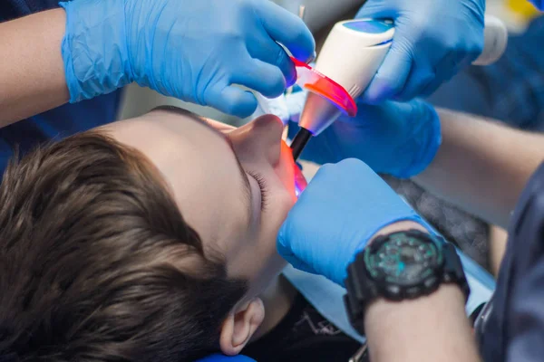 Um dentista e um assistente tratam os dentes de um jovem. Adolescente em odontologia . — Fotografia de Stock