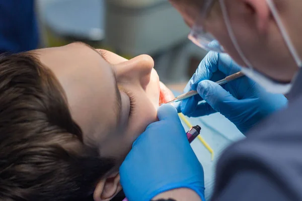 Tiener in een tandheelkundige kliniek. Een tandarts is tanden met gereedschappen behandelen. — Stockfoto