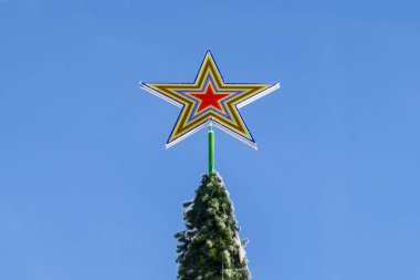 Noel ağacı. Mavi bulutsuz gökyüzüne karşı yeni yıl ağacının tepesindeki beş köşeli kırmızı bir yıldızın yakın çekimi. Şenlikli kış havası ve bayram süsü. Boşluğu kopyala.
