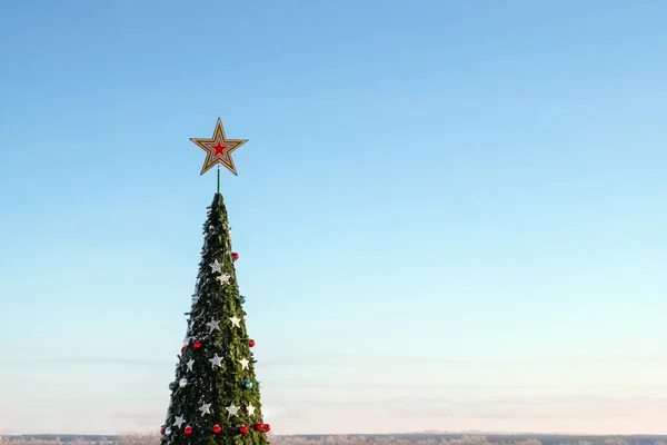 Árbol de Navidad. Humor festivo de Año Nuevo. La corona de un gran abeto con una estrella y juguetes contra un cielo azul sin nubes. Copiar espacio . —  Fotos de Stock
