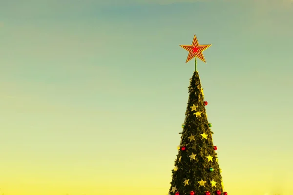 Árbol de Navidad. Humor festivo de Año Nuevo. La corona de un gran abeto con una estrella y juguetes contra un cielo azul sin nubes. Tinte amarillo soleado. Copiar espacio . —  Fotos de Stock
