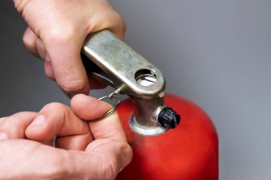 Erkek parmağı pimi çeker. Bir adam kırmızı yangın söndürücüden bir güvenlik halkası çıkarıyor. Yakın plan. İtfaiye yönetmeliği. Acil durum önlemi. Yüzeyin derinliği. Seçici odak.