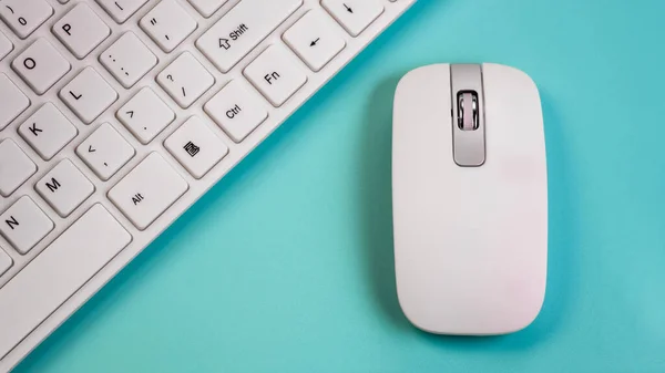 Bezdrátová myš leží vedle bílé klávesnice počítače. Modré pozadí. Detailní záběr. Koncept kancelářského manažera nebo počítačového salonu prodávajícího periferní zařízení. — Stock fotografie