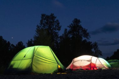 Akşam ormanının arka planında parlayan turist çadırları ve bulutlu mavi gökyüzü. Film sesi, tahıl, yüksek Iso. Turistler için gece çadırı. Seyahat, tatil ve turizm kavramı. Kopyalama alanı