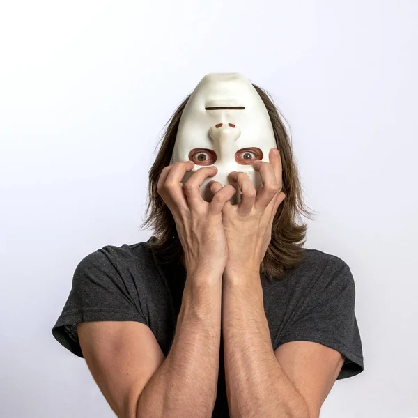 A man covers his face with a white mask upside down and tries to tear it off. The concept of personality crisis, fear, paranoia or mental disorders. Inverted world, eyes horror, loss of self-control. — Stock Photo, Image