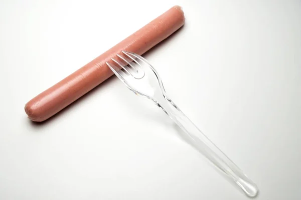 Sausage and a fork on a white background. Copy space. The concept of fast food, GMOs, hunger or lack of food. Environmental issue and the ban on plastic dishes. — Stock Photo, Image