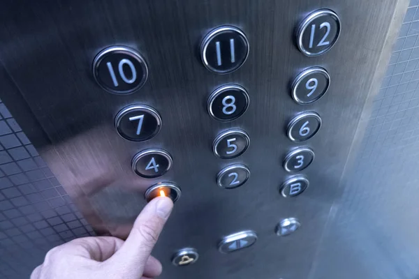 Tangan menekan tombol lift di lantai satu. Seorang pria di lift logam. Sebuah bangunan dua belas lantai. Fokus selektif. Bidang kedalaman yang dangkal. Kabur . Stok Gambar Bebas Royalti