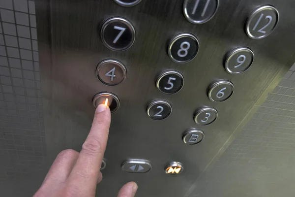 Seorang pria di lift logam. Sebuah bangunan dua belas lantai. Tangan menekan tombol lift di lantai satu. Fokus selektif. Bidang kedalaman yang dangkal. Kabur . Stok Foto