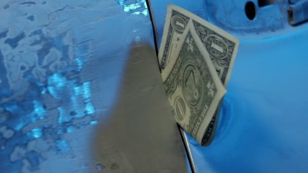 Una banconota da un dollaro incastrata nello spazio vuoto di un'auto non riparata. Primo piano. Il vento soffia. Tono blu. Povertà e stipendio basso in una stazione di servizio auto. Il concetto di basso salario lavoro Rifugiati. Questione sociale . — Video Stock