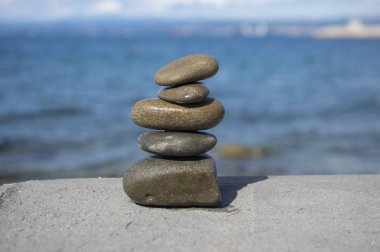 Five stones cairn tower, rock zen sculpture, brown beige pebbles and sea light blue background clipart