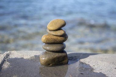Five stones cairn tower, rock zen sculpture, brown beige pebbles and sea light blue background clipart