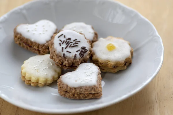 Gem și smântână umplut cookie-uri cu zahăr dulce glazură albă pe placă albă pe masă de lemn, grup de dulciuri de Crăciun — Fotografie, imagine de stoc