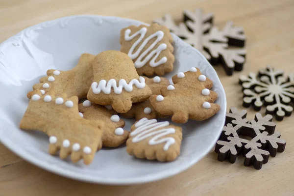 各种形状的圣诞姜饼放在木制桌子上的白盘上，一组简单的冬季糖果加冰块 — 图库照片