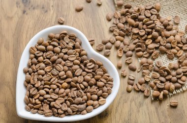 Beyaz kalp şeklinde tabağa ahşap masa kahve çekirdekleri.