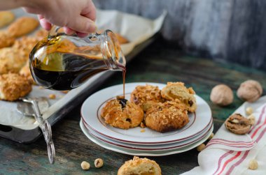 The woman is pouring grape molasses onto cookies with walnuts