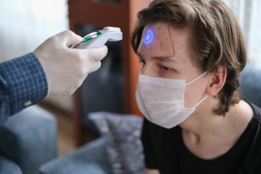 Baba, oğlunun sıcaklığını evinde kızılötesi termometreyle kontrol ediyor.