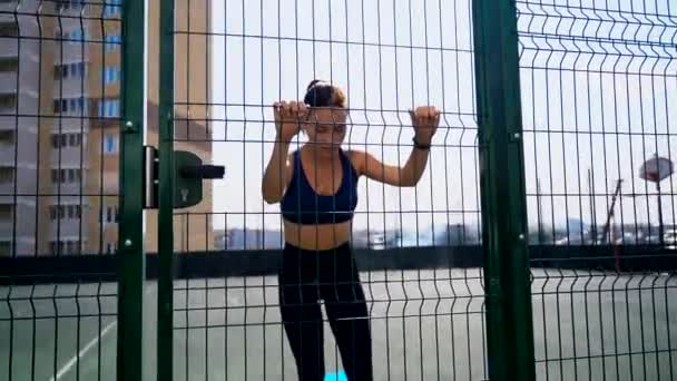 Girl on a basketball court performs an exercise. Leaving legs to the side while standing using fitness rubber band. Exercises for the buttocks and hips with a fitness gum. — Stock Footage Girl on a basketball court performs an exercise. Leaving legs to the side while standing using fitness rubber band. Exercises for the buttocks and hips with a fitness gum. Royalty Free Stock Video