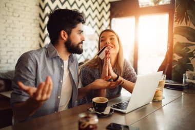Genç çift kafede dizüstü bilgisayar ile online alışveriş yaparken. Karışık erkek. Kız erkek pahalı hediye almak isteyen eller yalvarıyor şey.