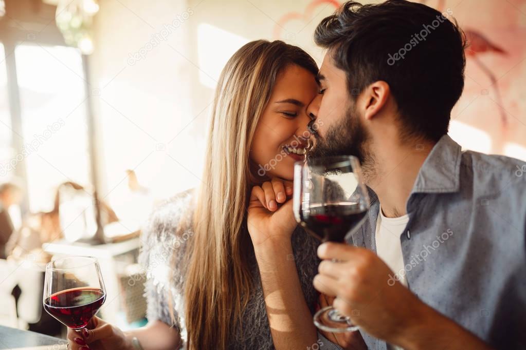 Close-up of an attractive couple. Boyfriend kissing his girlfriend in nose. Couple drinking red wine and celebrating anniversary or Valentine's day.