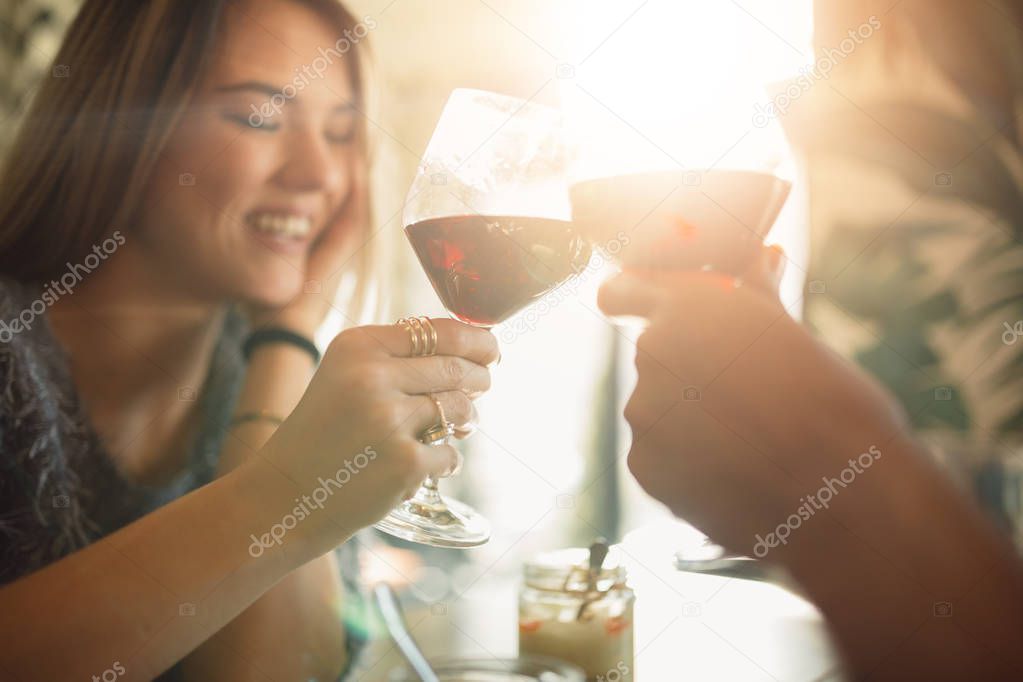 Couple clink glasses with red vine at date, celebrating anniversary or Valentine's day.