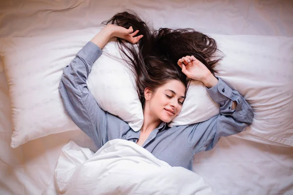 Pretty young woman on bed in modern apartment smiling after wake up.