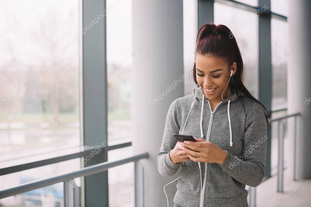 Fit girl dressed in sporty wear listening to the music or texting after workout. Copy space.