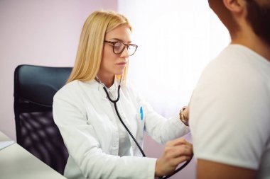 Doktor muayene hasta stetoskop tıbbi ofis ile. Doktor stetoskop sınav adam hasta kalp için kullanma. Kadın doktor portresi bir hasta stetoskop ile inceliyor..