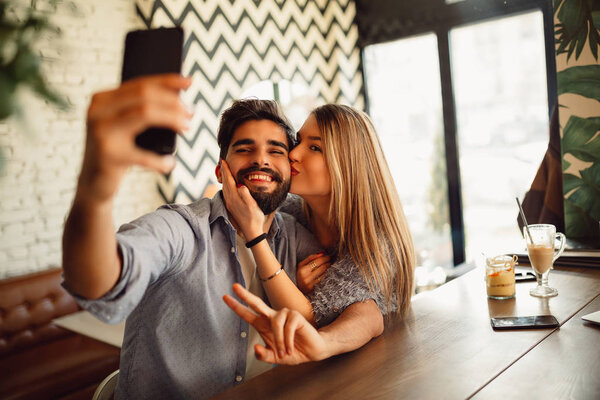 Young fashion lover couple at beginning of love story. Handsome man taking selfie with pretty woman at fashion coffee bar. Relationship concept with nice boyfriend and girlfriend.