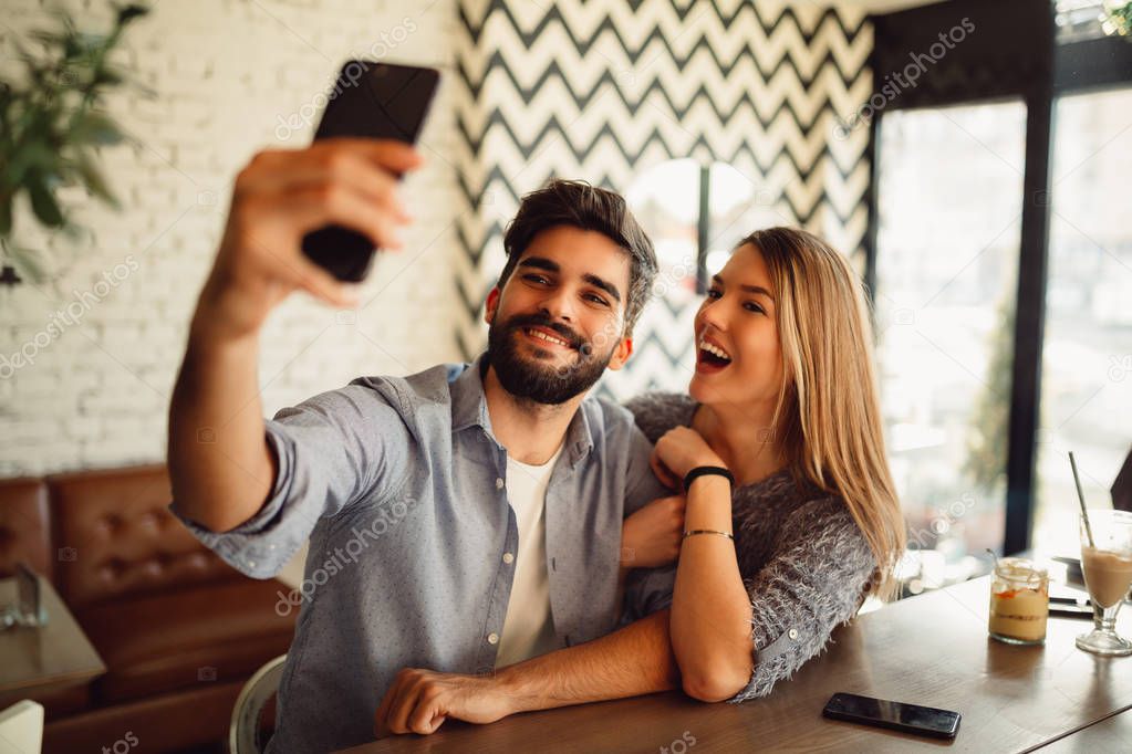 Young attractive couple making selfie in cafeteria.