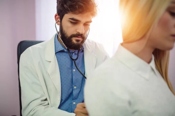 Doktor muayene hasta stetoskop tıbbi ofis ile. Doktor stetoskop sınav adam hasta kalp için kullanma. Yakışıklı erkek doktor portresi bir hasta stetoskop ile inceliyor..
